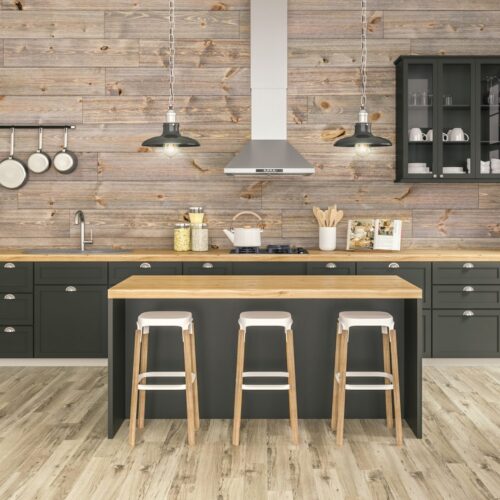 Modern kitchen with gray-brown barnwood plank accent wall, dark cabinetry, light wood island with three stools, pendant lights, and stainless range hood.