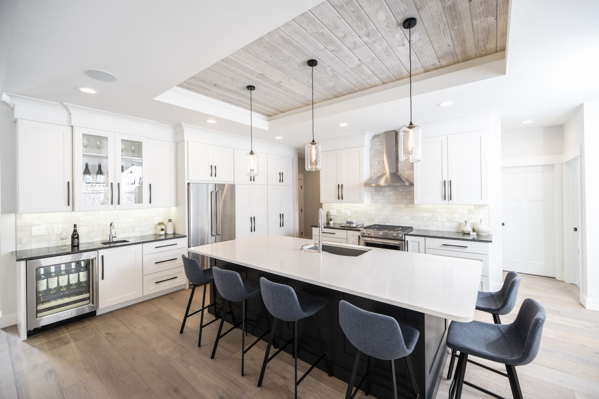 Modern white kitchen with large island, blue upholstered stools, glass pendant lights, and a recessed tray ceiling finished with Easy BarnWood “Traditional White” planks.