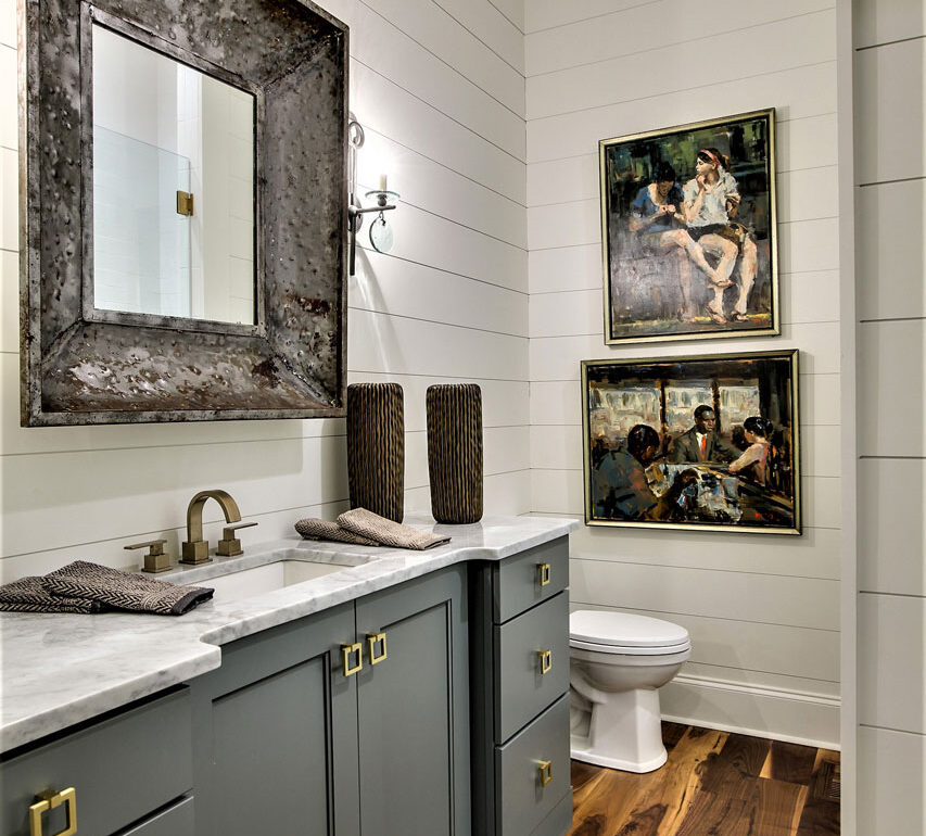 Powder room with white smooth pine finger-joint horizontal plank walls, gray vanity with brass pulls, large rustic framed mirror, and dark wood floor.