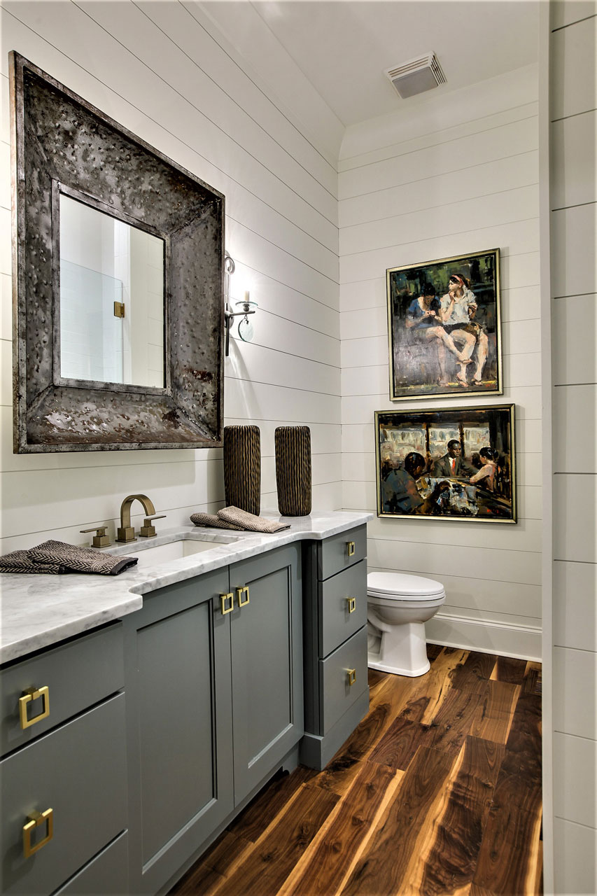 Powder room with white smooth pine finger-joint horizontal plank walls, gray vanity with brass pulls, large rustic framed mirror, and dark wood floor.