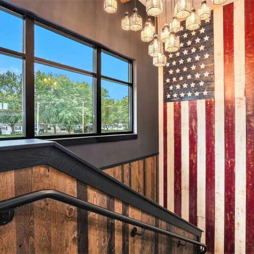 Stairwell landing with reclaimed wood wainscoting, large wooden American flag wall art, pendant lights, and black-framed windows.
