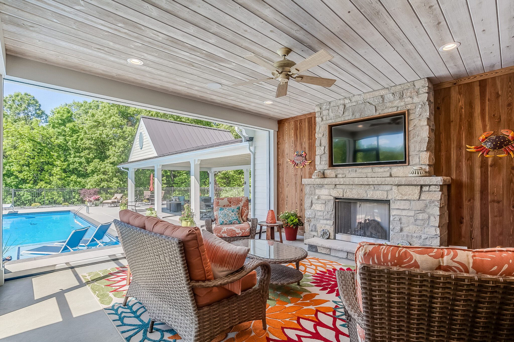 Covered patio with Easy BarnWood Traditional White plank ceiling and matching wall boards, stone fireplace with TV, and pool view.