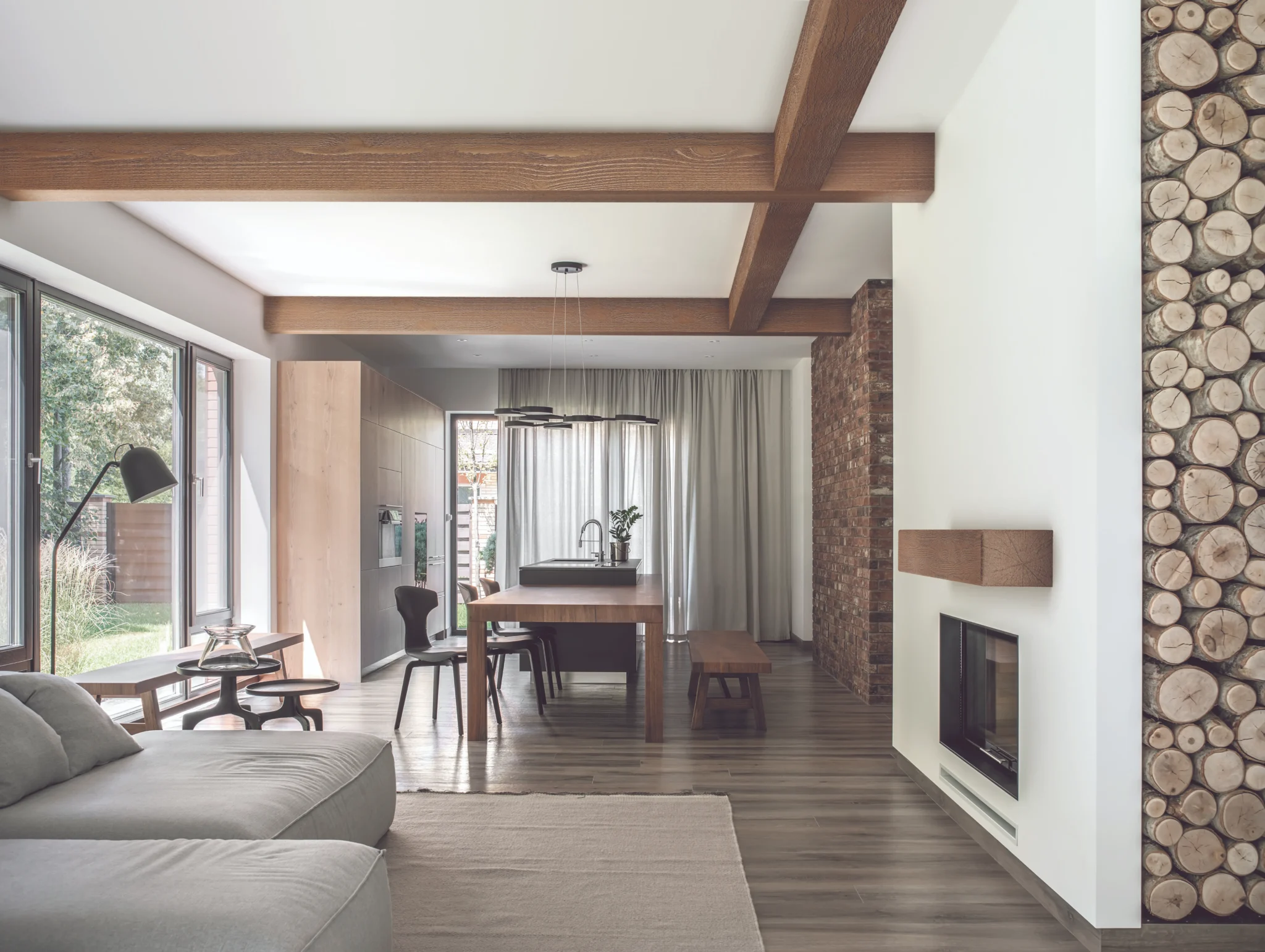 Modern living room with rough-sawn wood ceiling beams, a white fireplace with wood mantel, and an open dining area with large glass doors.