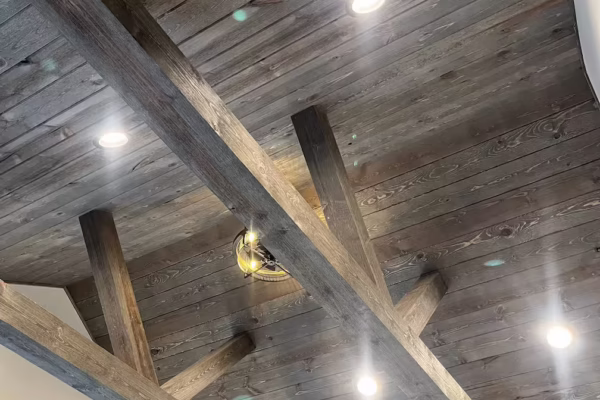 Dark wood plank ceiling with exposed cross beams and recessed can lights in a rustic-modern interior.
