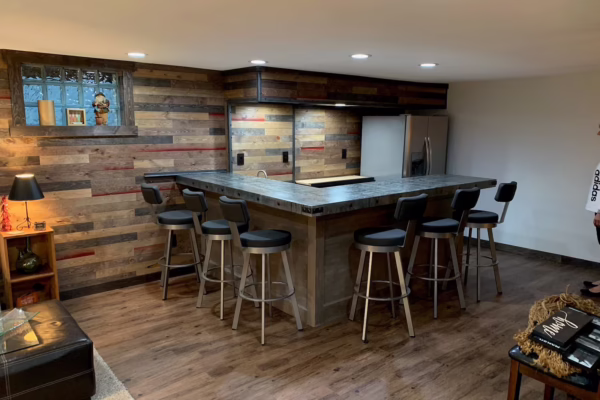 Reclaimed wood plank accent walls in a finished basement bar with an L-shaped counter and stools.