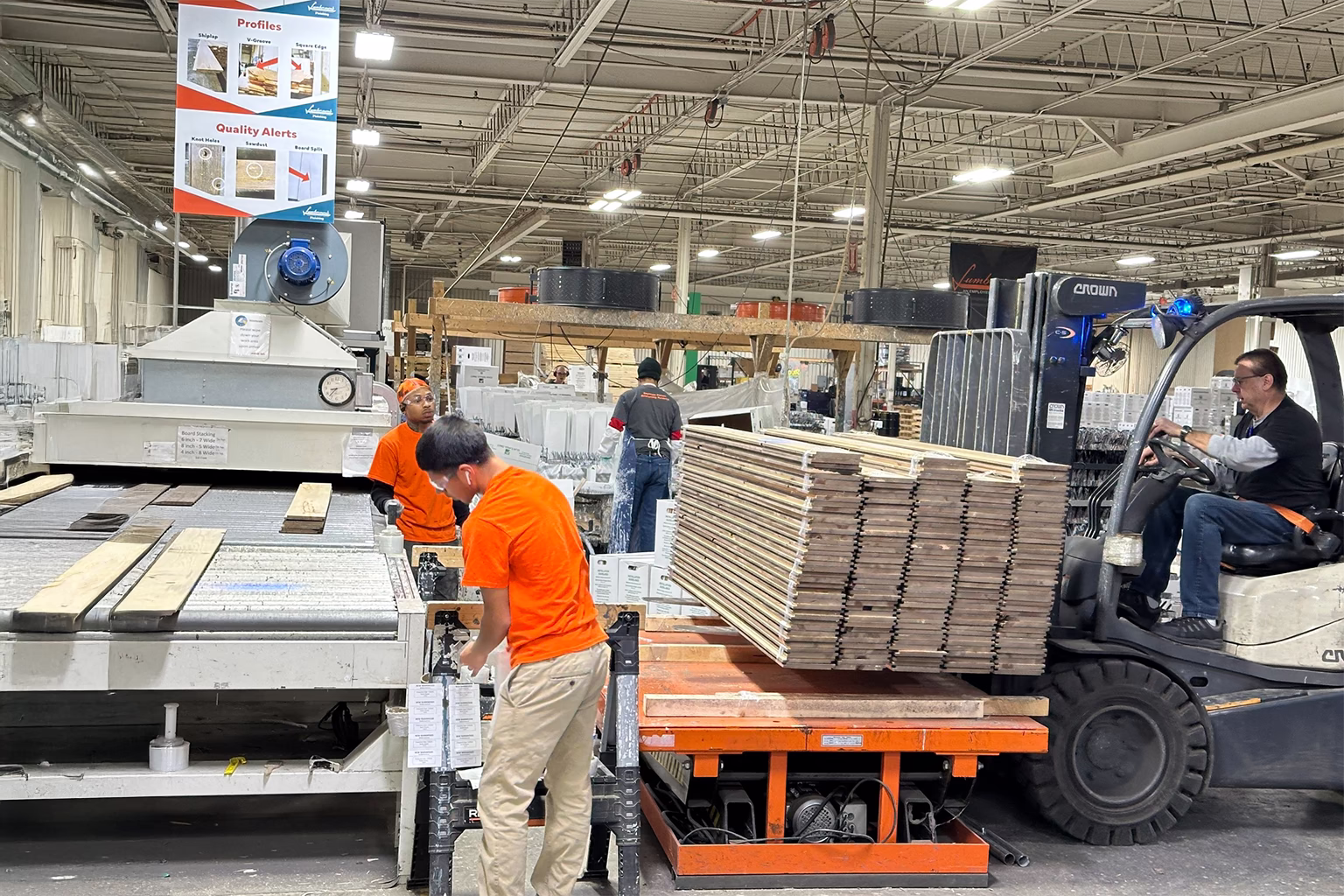 Factory production line with workers and a forklift moving stacked wood boards through the facility.