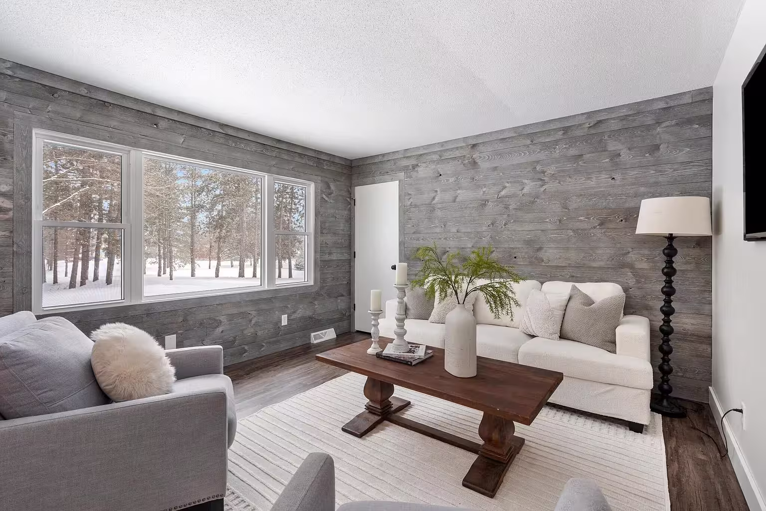 Living room with weathered gray horizontal wood plank walls, large windows, and a white sofa around a wood coffee table.