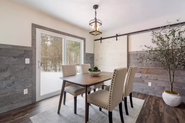 Dining room with gray wood plank wainscoting, white upper walls, and a white sliding barn door beside a large glass patio door.