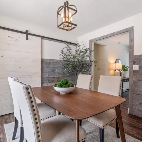 Dining room with gray wood plank wainscoting and white upper walls, featuring a light wood sliding barn door on a black rail.