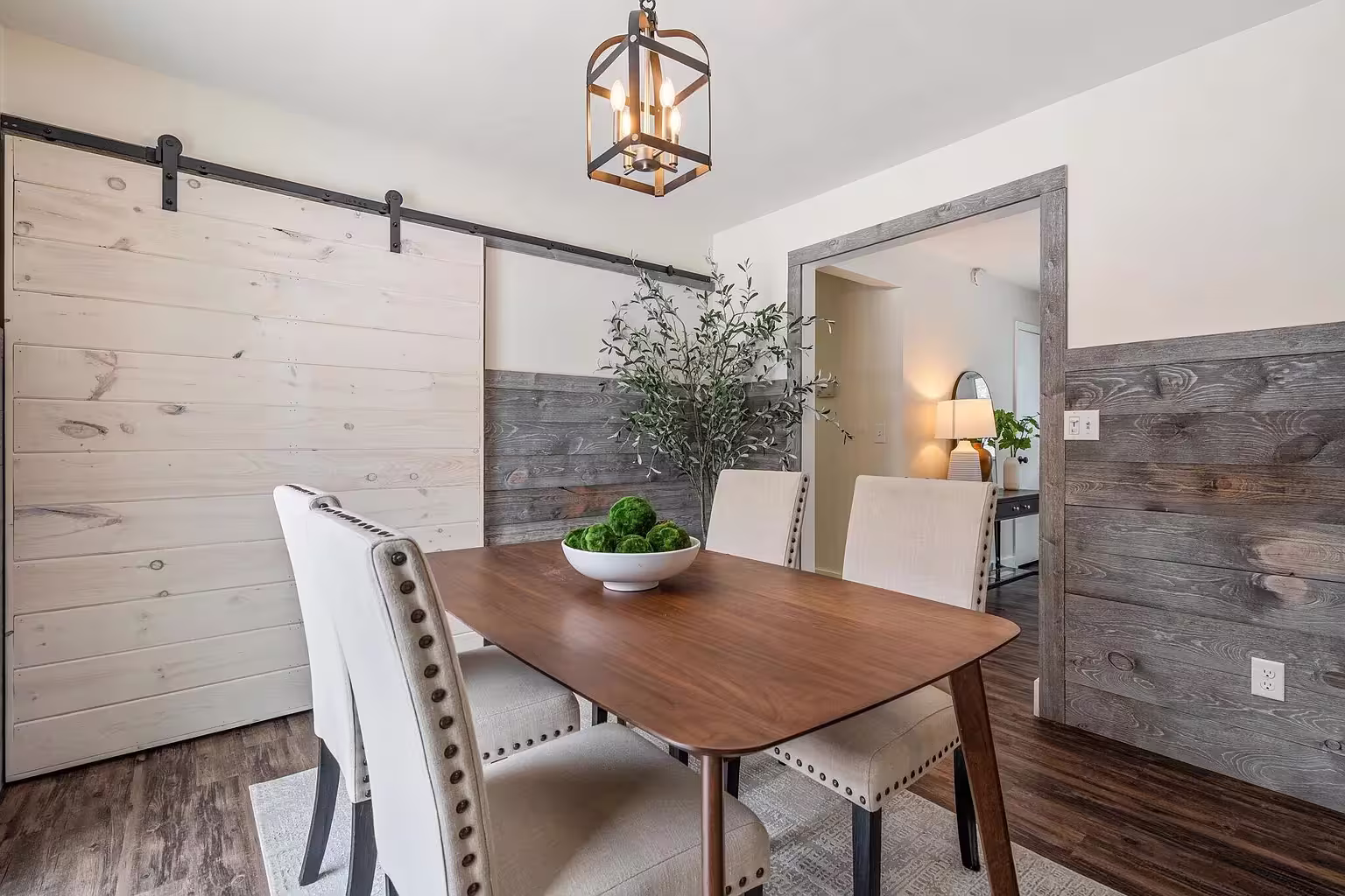 Dining room with gray wood plank wainscoting and white upper walls, featuring a light wood sliding barn door on a black rail.